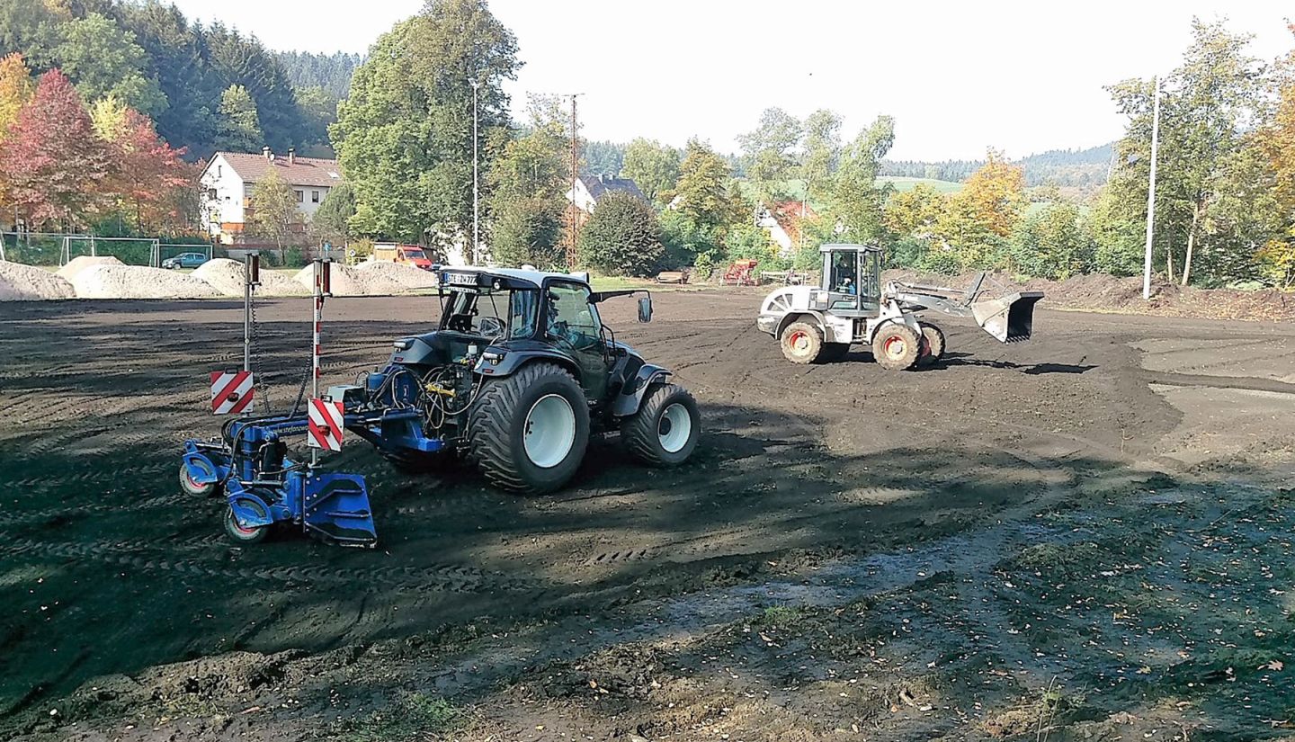 Ein Traktor mit angehängtem Planierschild und ein Radlader legen einen neuen Sportplatz an