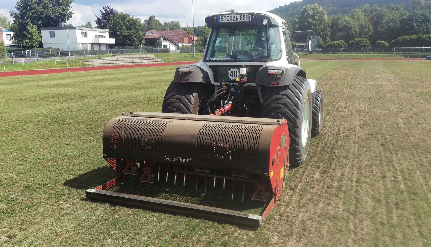 Ein Traktor mit Spezialgerät beim Aerifizieren eines Sportplatzes